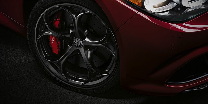 Close-up of an Alfa Romeo wheel with dark rims and red brake calipers.