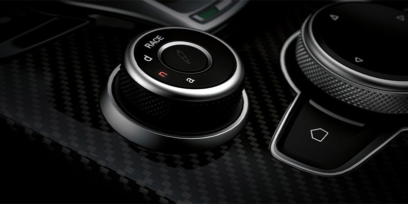 Close-up of an Alfa Romeo DNA drive mode selector on carbon fiber.