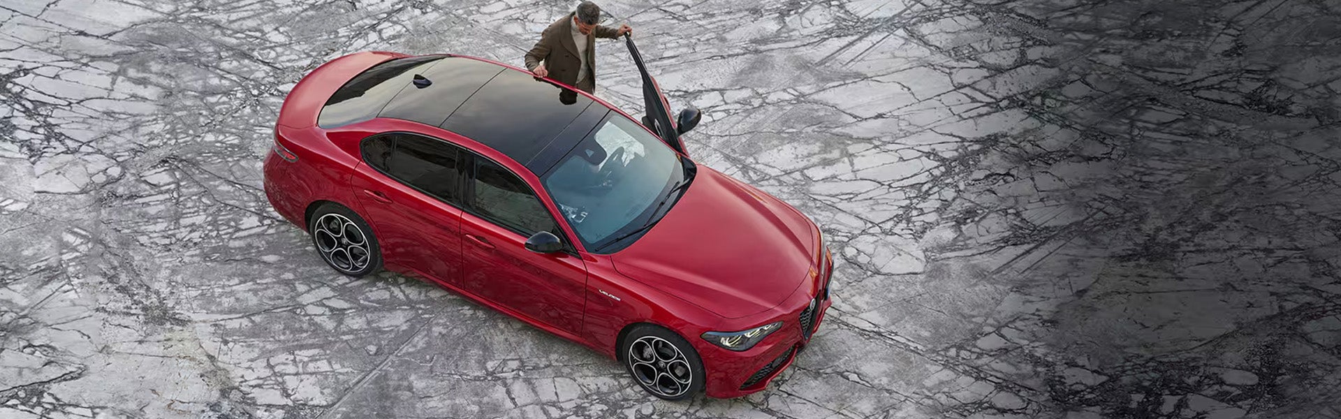 High-angle view of a red Alfa Romeo Giulia parked on cracked marble.