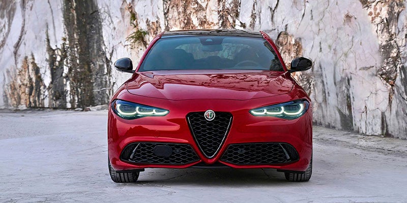 Front view of a red Alfa Romeo Giulia on a coastal road.