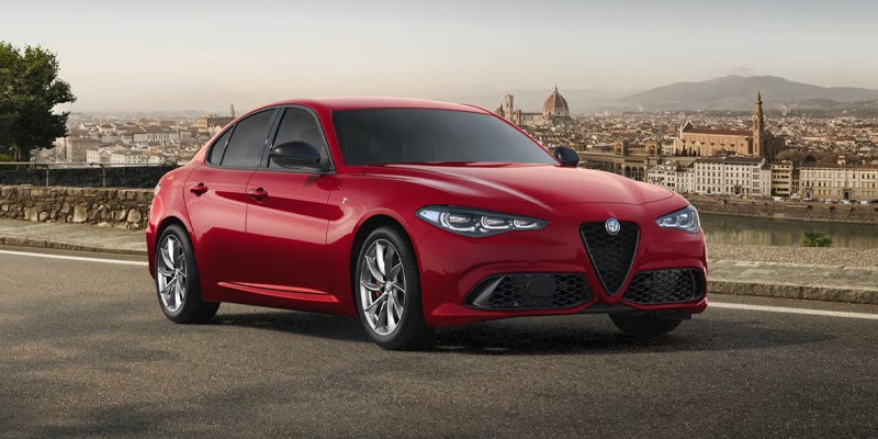 Red Alfa Romeo Giulia parked with a scenic European city background.