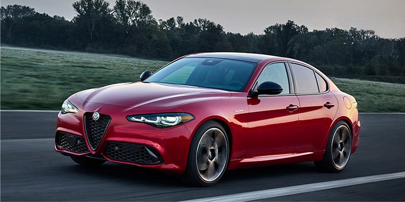 A red Alfa Romeo Giulia driving on a road at dawn