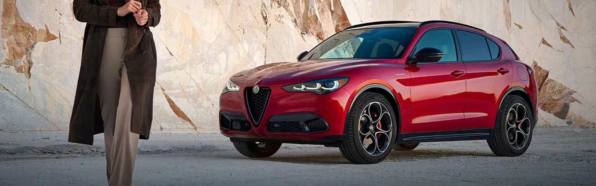 Red Alfa Romeo SUV parked in front of a marble quarry wall.