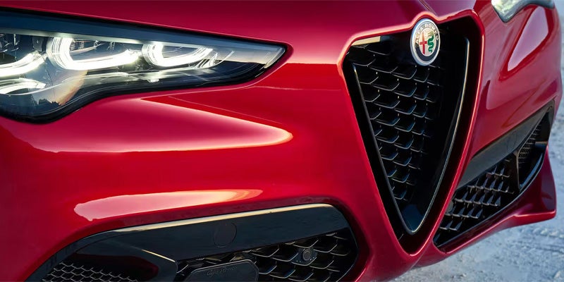 Close-up of the front grille and headlight of a red Alfa Romeo.