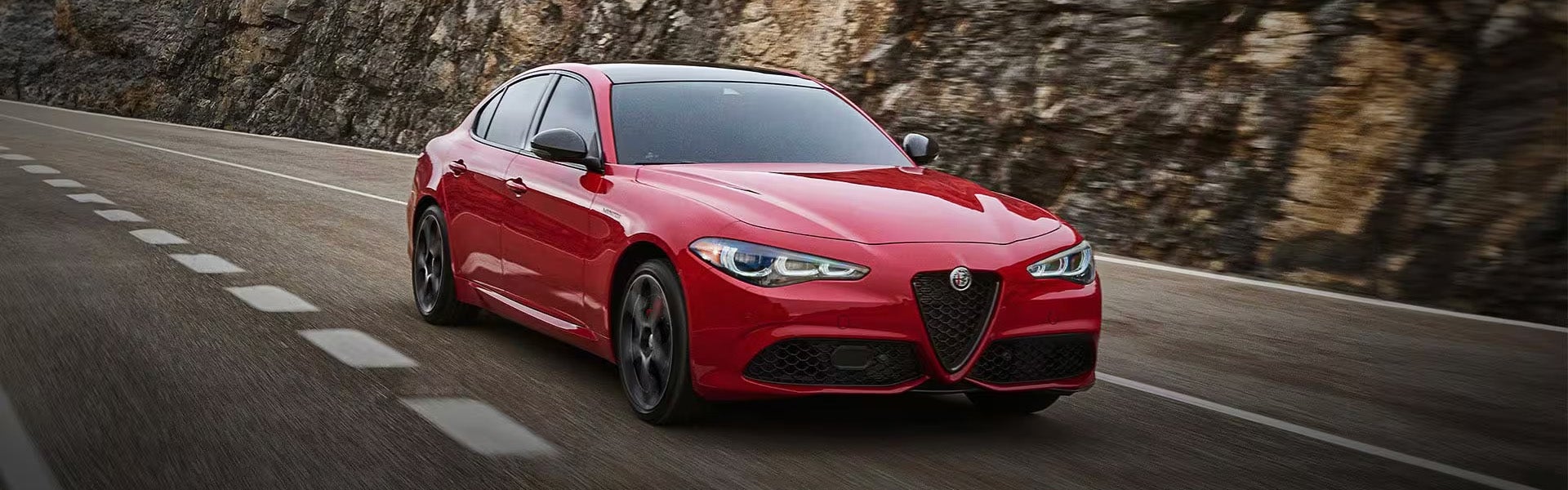 A red Alfa Romeo Giulia sedan driving on a mountain road
