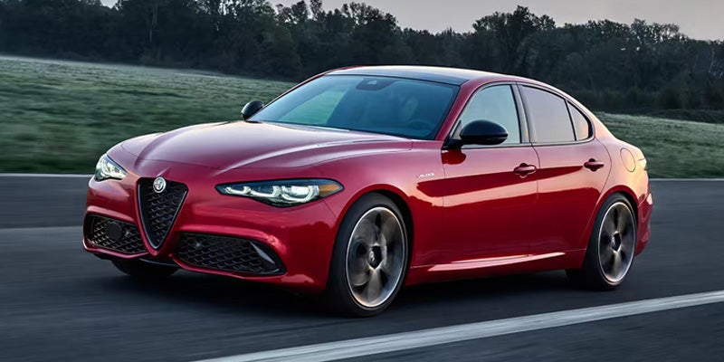A red Alfa Romeo Giulia driving on a road at dawn.