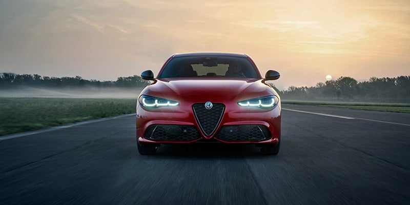 Red Alfa Romeo Giulia driving on a track during sunset.