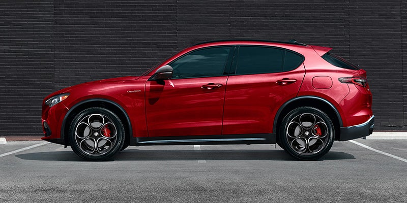 Side profile of a red Alfa Romeo Stelvio parked against a brick wall.