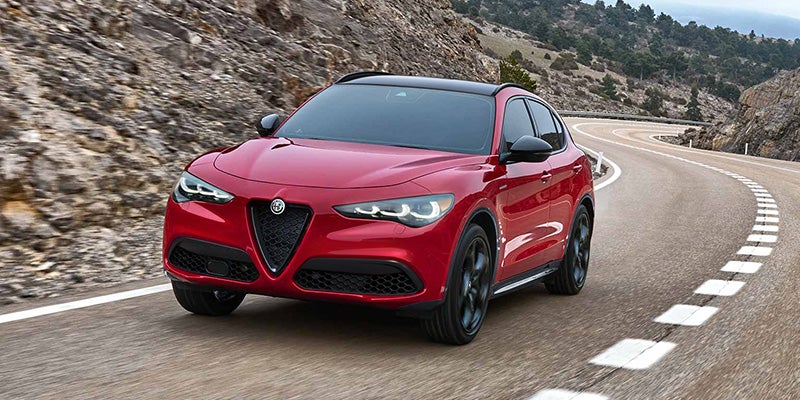 Red Alfa Romeo Stelvio driving on a winding paved mountain road.