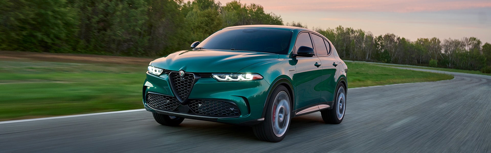 Green Alfa Romeo Tonale SUV driving on a winding road at sunset