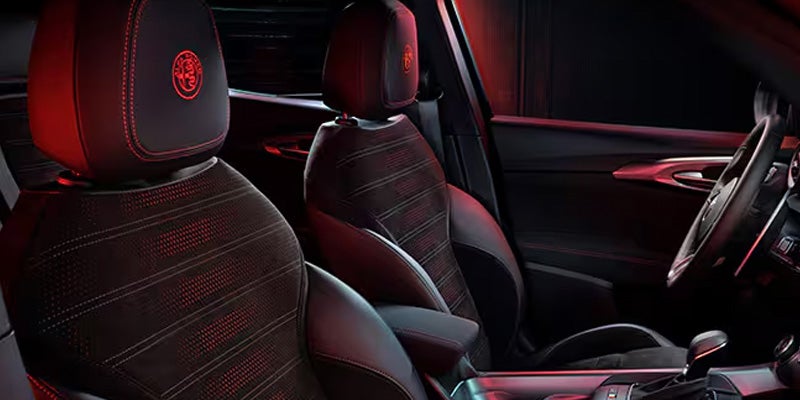 Interior view of dark car seats with red embroidered Alfa Romeo logos.